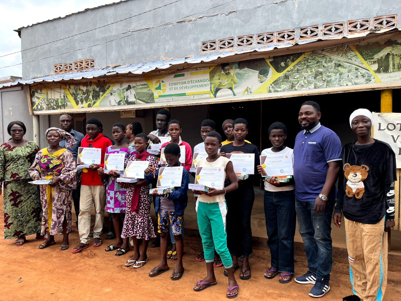 Groupe de jeunes et encadrants avec leurs attestations et kits scolaires devant le siège de CED